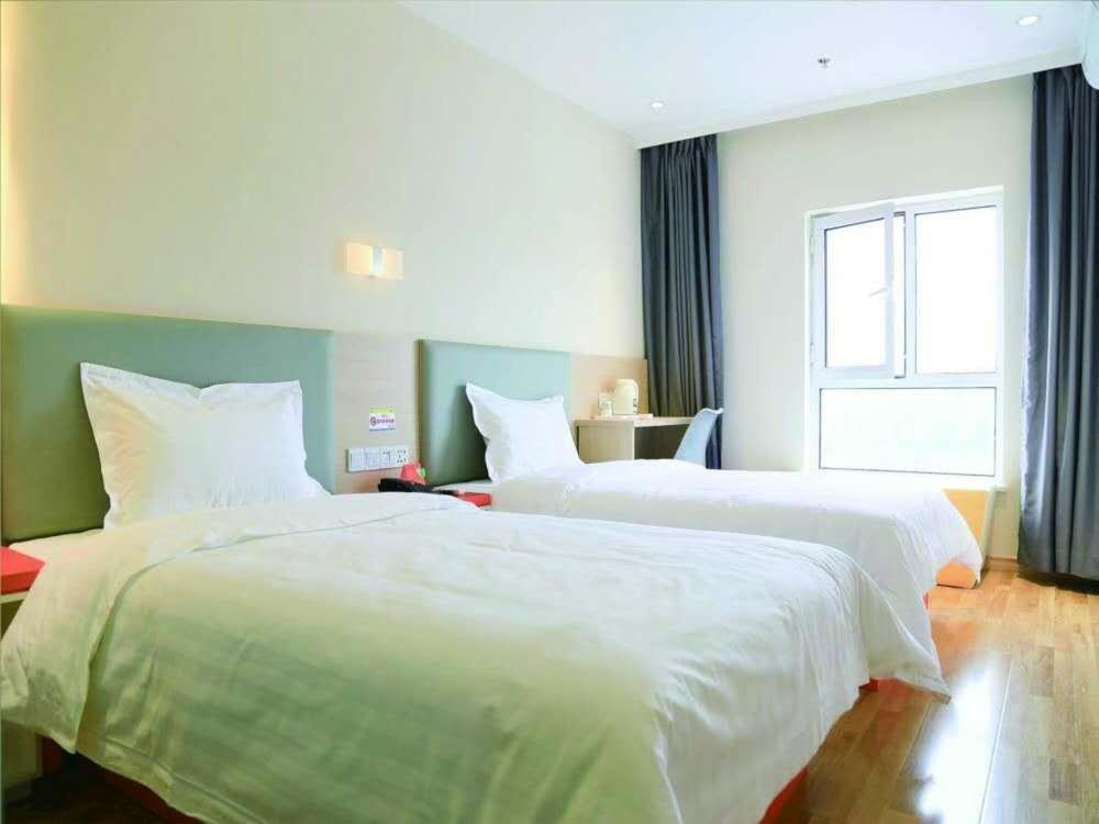 2 camas blancas en una habitación con ventana en 7Days Inn Ji'nan Changqing University Ginza Commercial Street Branch, en Jinan