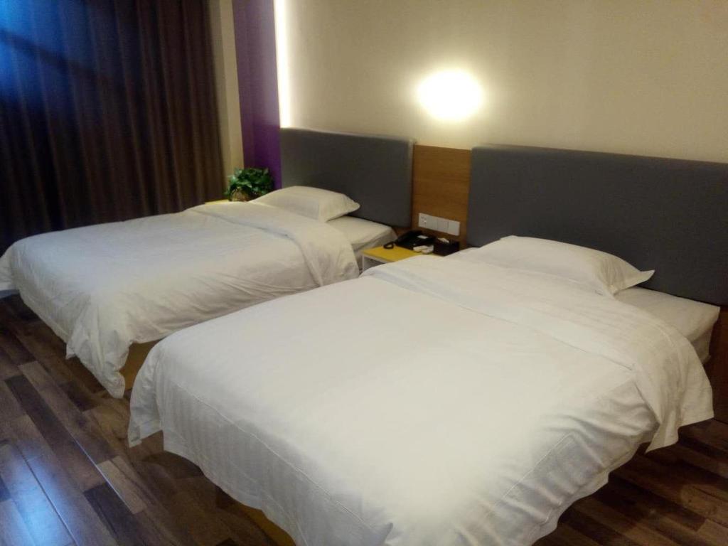 two beds in a hotel room with white sheets at 7Days Inn Xiaoyi People's Hospital Branch in Yaopu