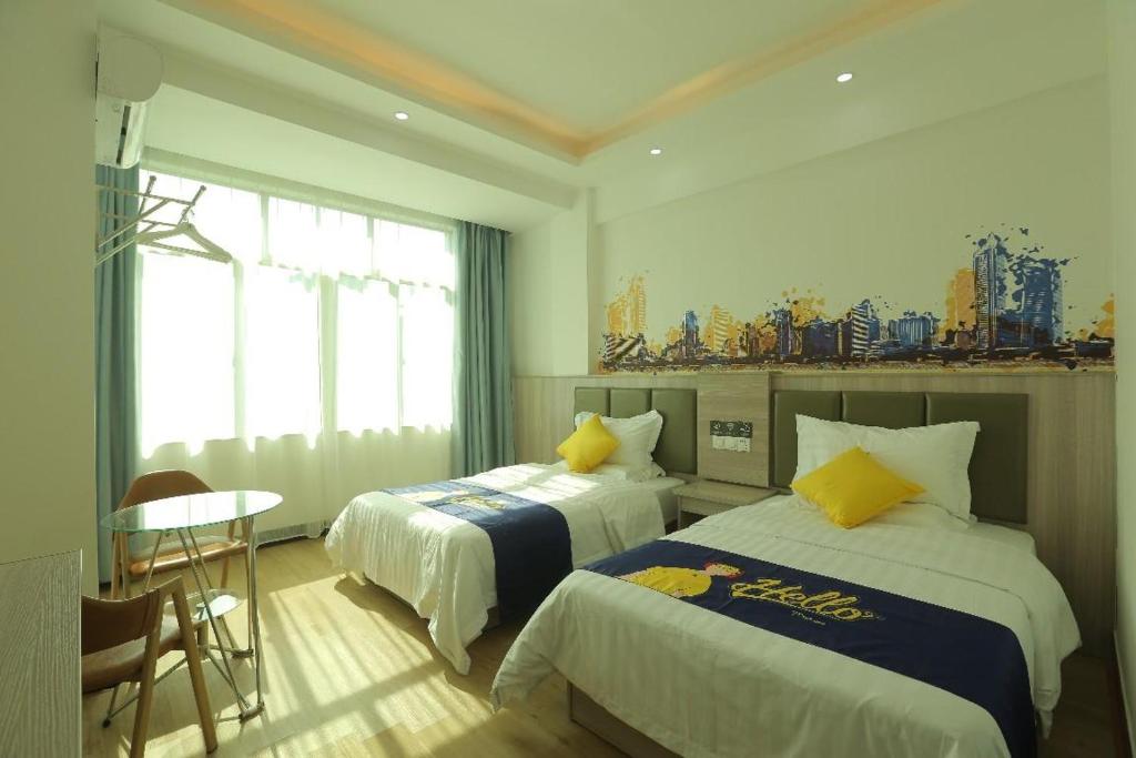 a bedroom with two beds and a table and a window at 7 Days Inn Haikou East Train Station North and South Fruit Market Fengxiang Road Branch in Haikou