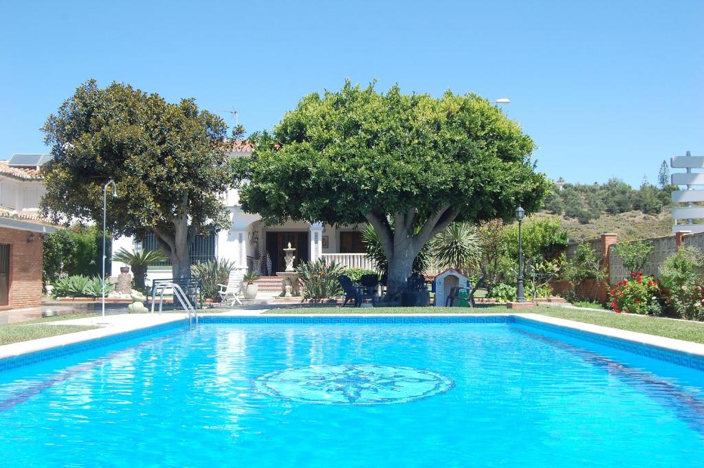 una gran piscina azul con árboles y una casa en Villa Maria Teresa, en Benajarafe
