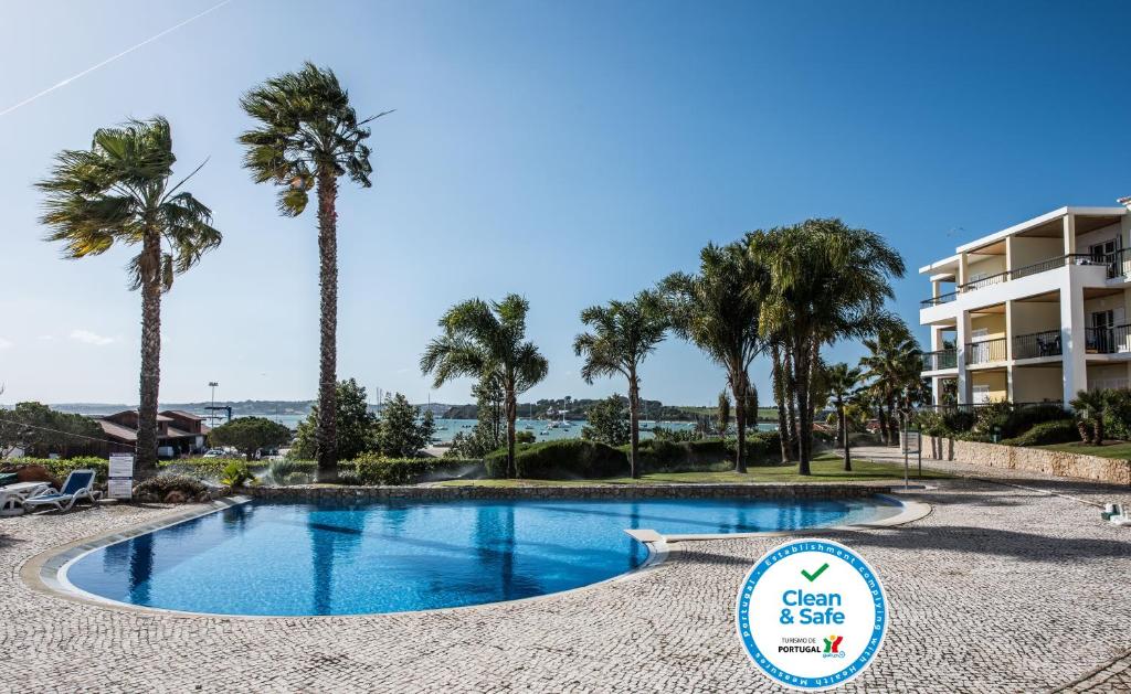 Una piscina con palmeras y un edificio. en Clube Alvor Ria - Prime Residence, en Alvor