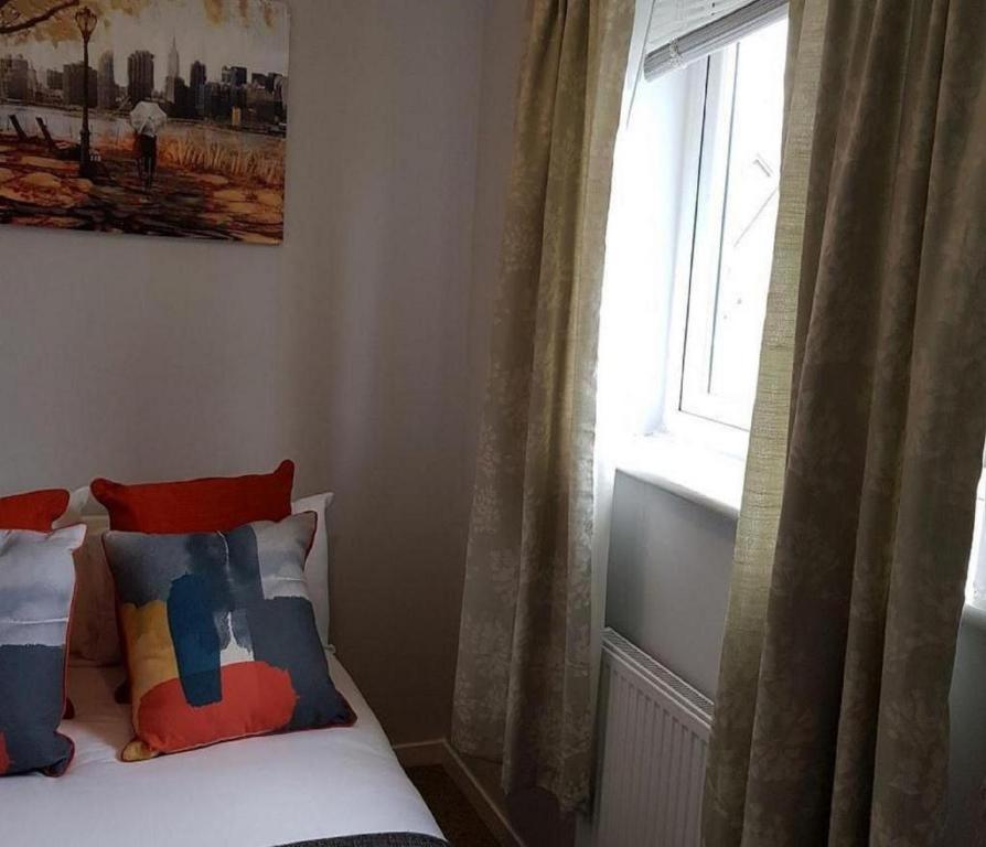 a bedroom with a window and a bed with colorful pillows at Ravenhill House - Huku Kwetu Luton & Dunstable Spacious 4 Bedroom Detached House -Free Parking-Field View-Affordable Group Accommodation - Business Travellers in Luton