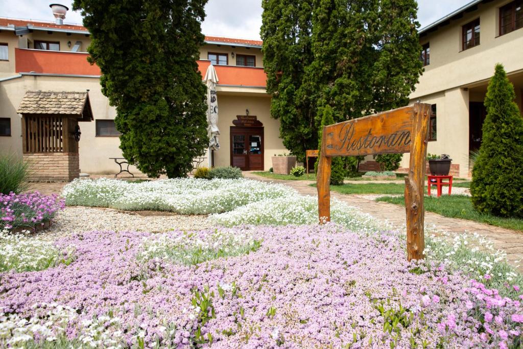 a sign in a garden with purple and white flowers at Hotel Lug in Osijek