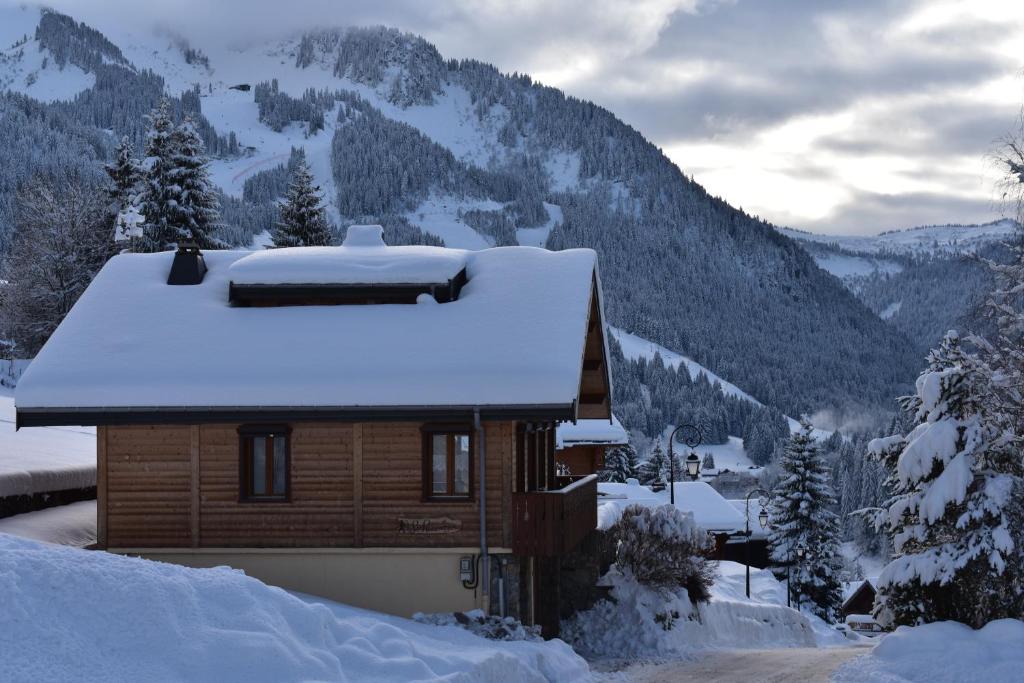 a house covered in snow with mountains in the background at Chalet le Petit Ramoneur in Châtel