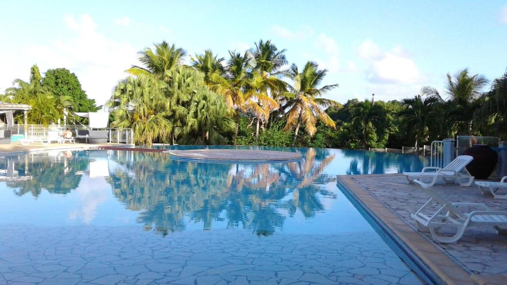 a swimming pool with two chairs and palm trees at Appartement moderne à Saint-François 90 m² avec piscine partagée in Saint-François