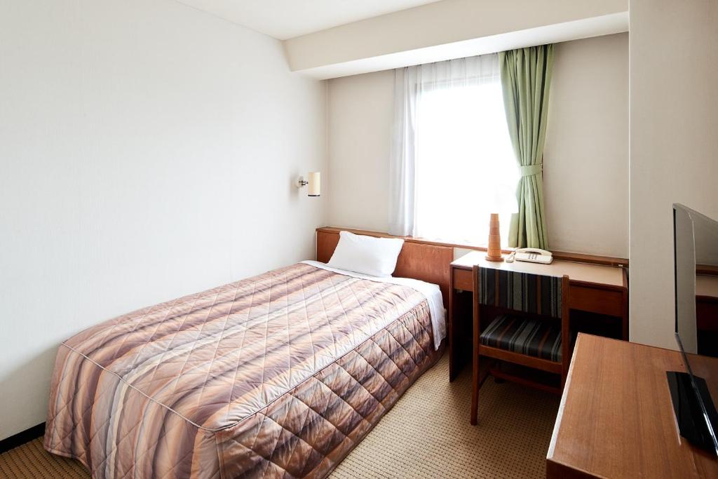 a hotel room with a bed and a desk and a window at Marroad Inn Tokyo in Fuchu