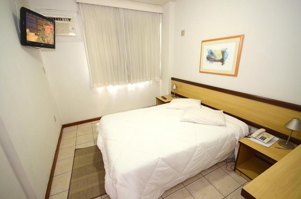um quarto com uma cama branca e uma televisão em Solar Flat Hotel em Juiz de Fora