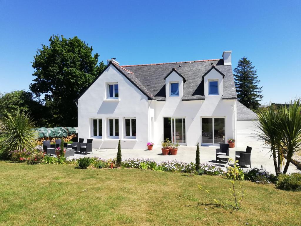 a white house with black chairs on a lawn at Jolie maison près de la mer au calme Seaside Country Cottage in La Forêt-Fouesnant