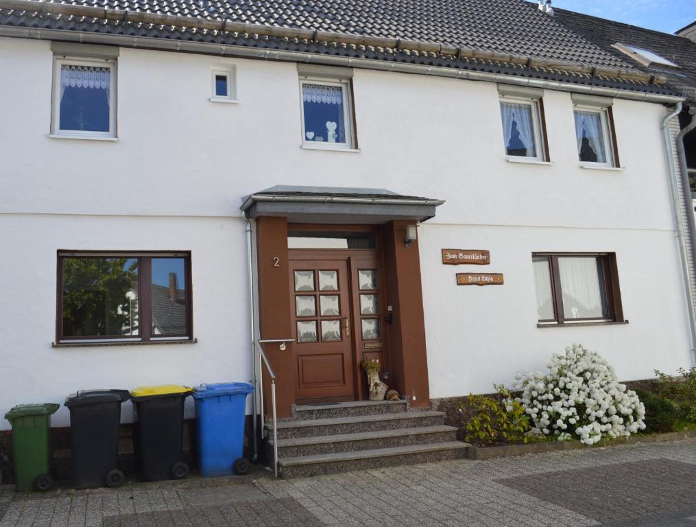 a white house with a brown door and two trash cans at Ferienwohnung Käthchen in Medebach
