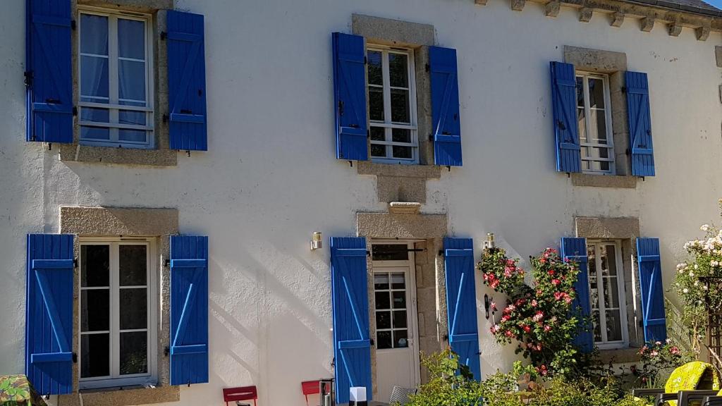 a white building with blue shuttered windows and flowers at Nuances bretonnes in Elliant