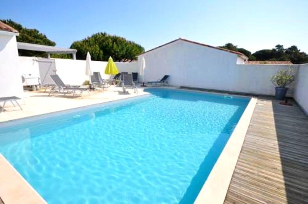 einen blauen Pool mit einer Holzterrasse und Stühlen in der Unterkunft Maison de 2 chambres a Le Bois Plage en Re a 400 m de la plage avec piscine partagee terrasse amenagee et wifi in Le Bois-Plage-en-Ré
