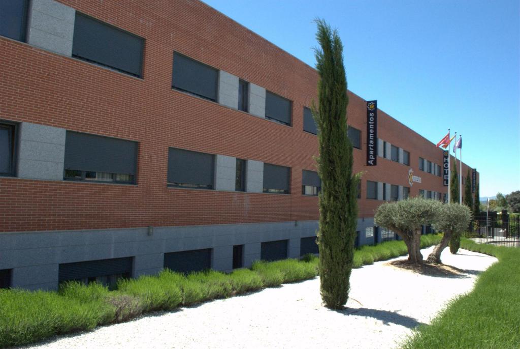 budynek z czerwonej cegły z dwoma drzewami przed nim w obiekcie Hotel-Apartamentos Tartesos w mieście Las Rozas de Madrid