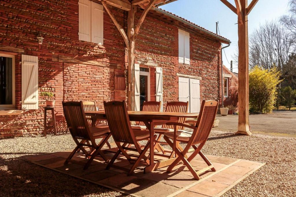 une table et des chaises en bois devant un bâtiment en briques dans l'établissement Gîte rural Aqui-naut, à Montesquieu-Volvestre