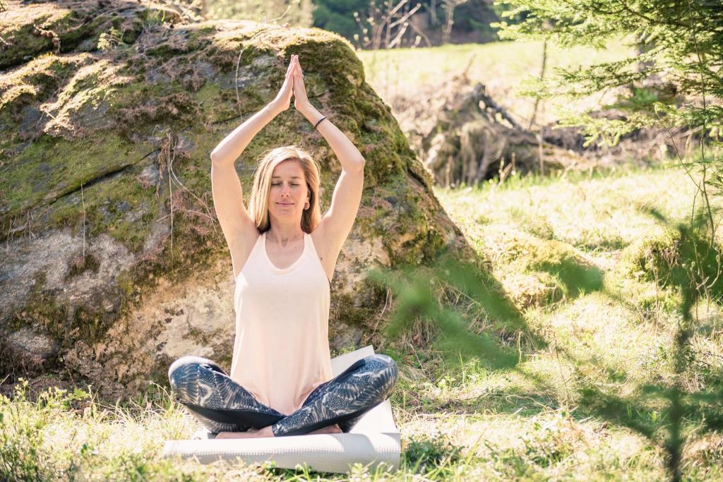a woman sitting in a yoga pose in front of a rock at Hôtel Magrappé in Veysonnaz