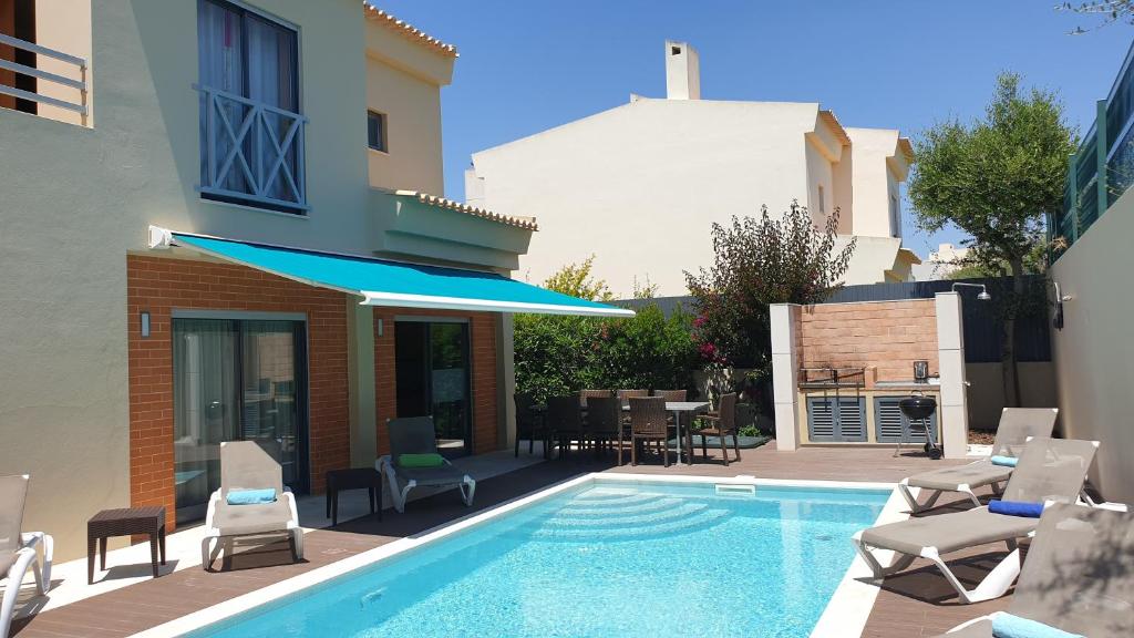 a swimming pool with chairs and a table and a building at Luxury Villa Corcovada Nicole with privat heated pool in Albufeira