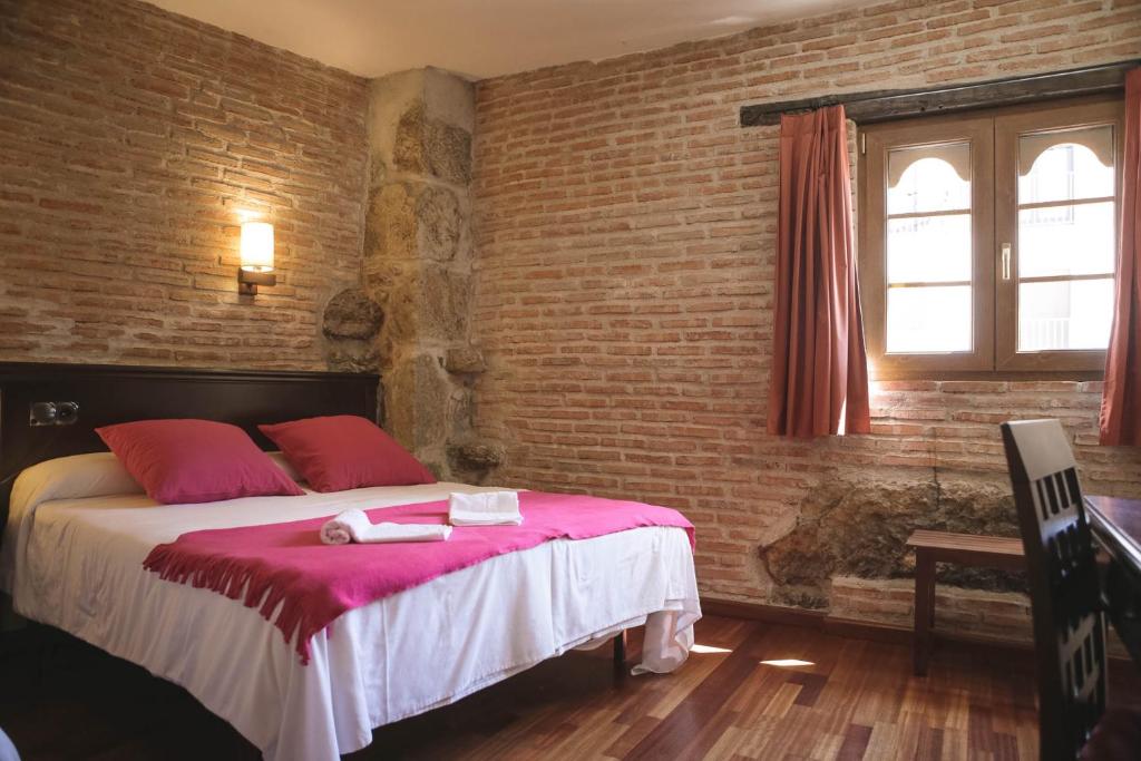 1 dormitorio con 1 cama con almohadas rojas y pared de ladrillo en Hospedium Hotel La Fuente, en Candelario