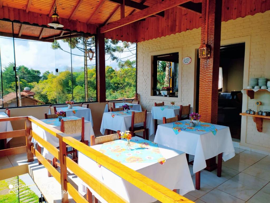 um restaurante com mesas e cadeiras brancas e janelas em Pousada Bosque em Monte Verde