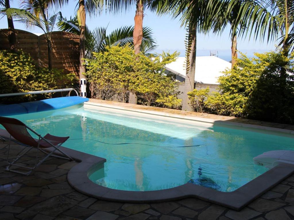 a swimming pool with a chair and palm trees at Villa de 2 chambres avec vue sur la mer piscine privee et jardin clos a Le Tampon in Le Tampon