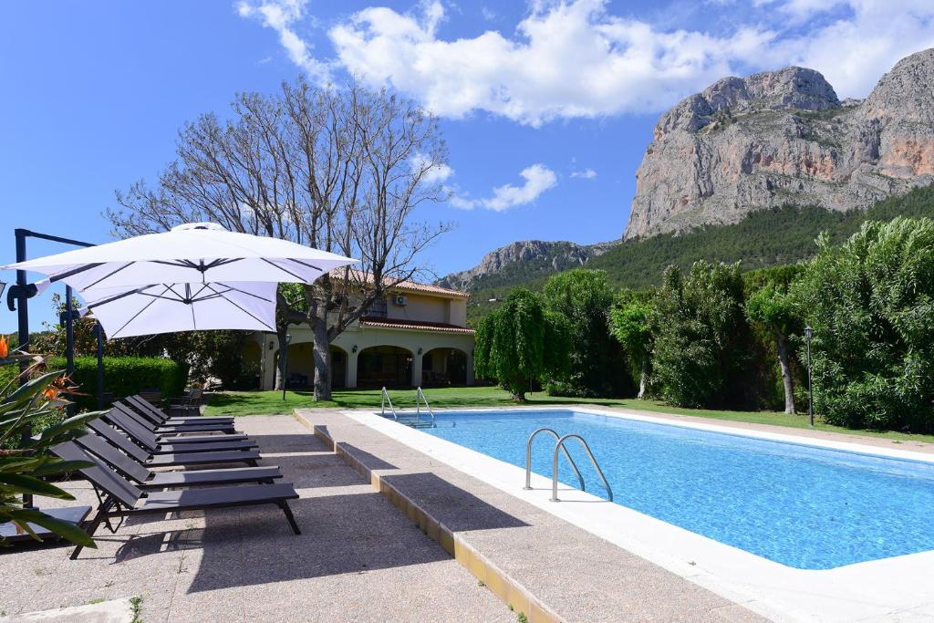 a pool with chairs and an umbrella next to a building at Villa Bovalar in Polop