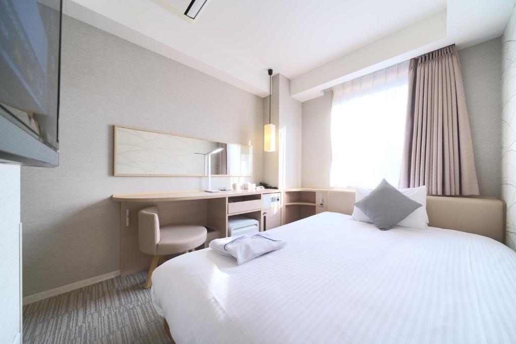 a hotel room with a large white bed and a desk at Meitetsu Inn Hamamatsucho in Tokyo