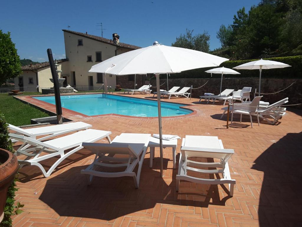 una piscina con mesas y sillas blancas y una sombrilla en Rocca Palazzaccio, en Impruneta
