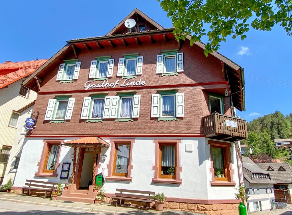 un bâtiment marron et blanc avec bancs devant lui dans l'établissement Schwarzwaldgasthaus Linde, à Tennenbronn