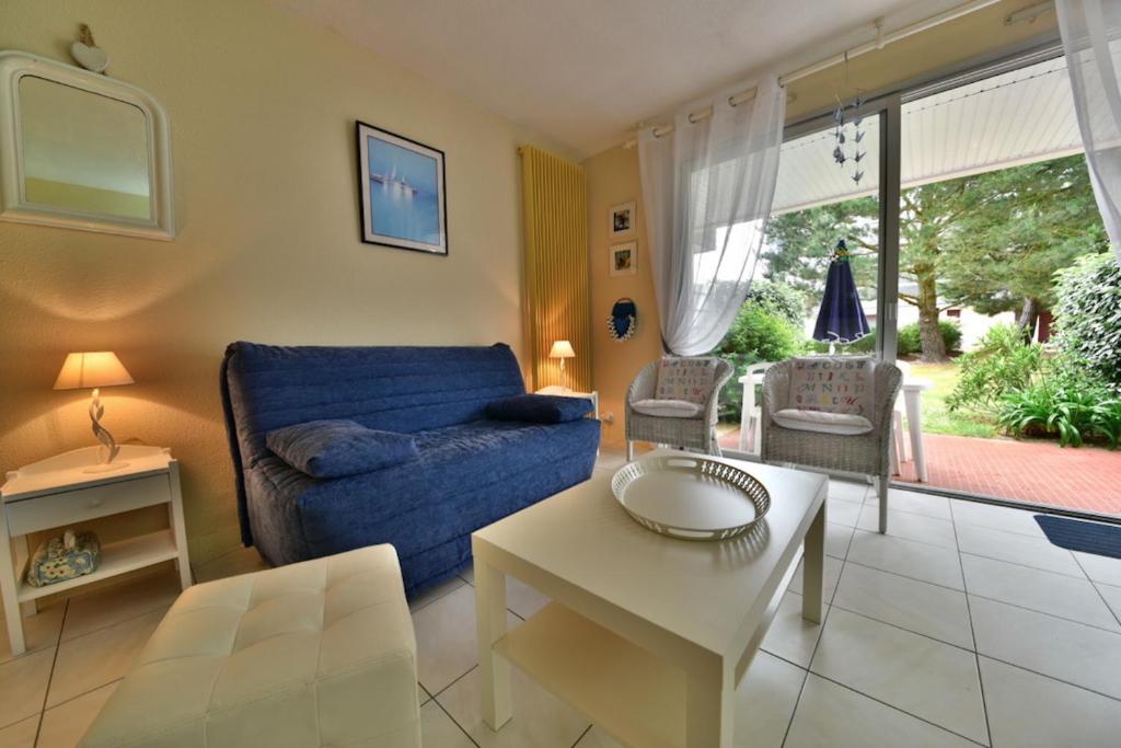 ein Wohnzimmer mit einem blauen Sofa und einem Tisch in der Unterkunft Residence Legenese - Studio COSY avec belle TERRASSE en REZ de JARDIN - 150m PLAGE in Carnac-Plage