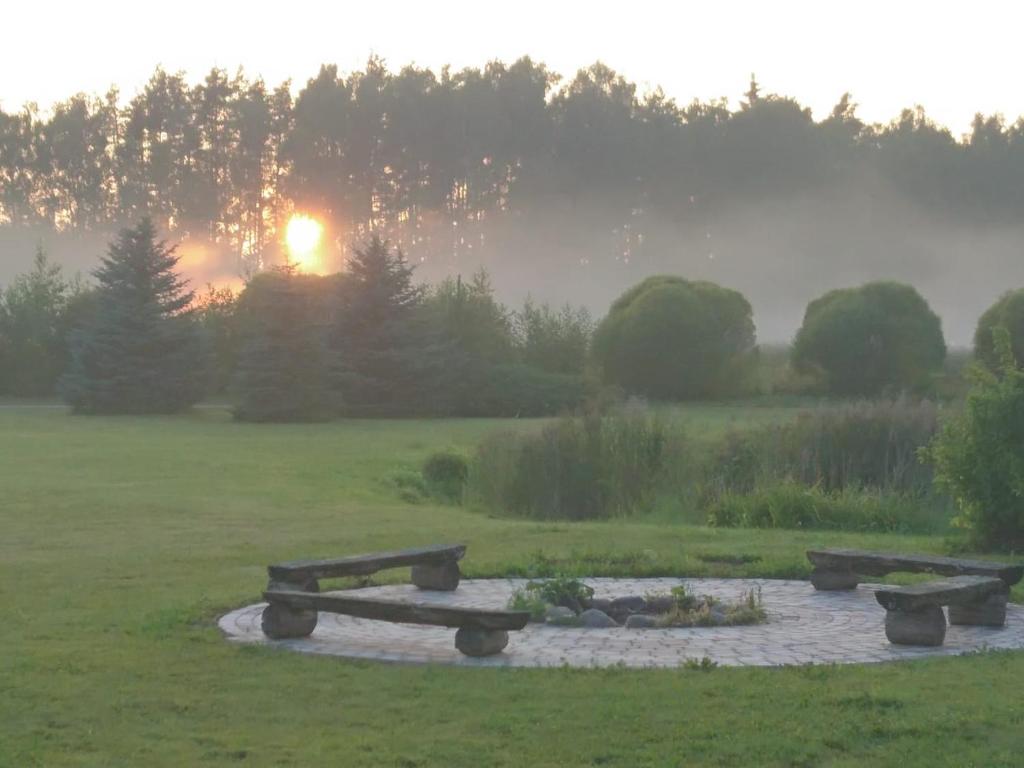 un banco de parque en un campo con la puesta de sol en el fondo en Līčupes, en (( Strēli ))