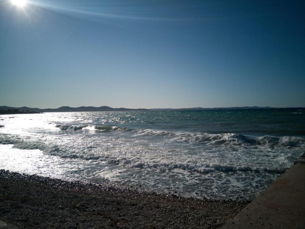 a beach with the sun shining on the water at Apartments Roncevic in Zadar