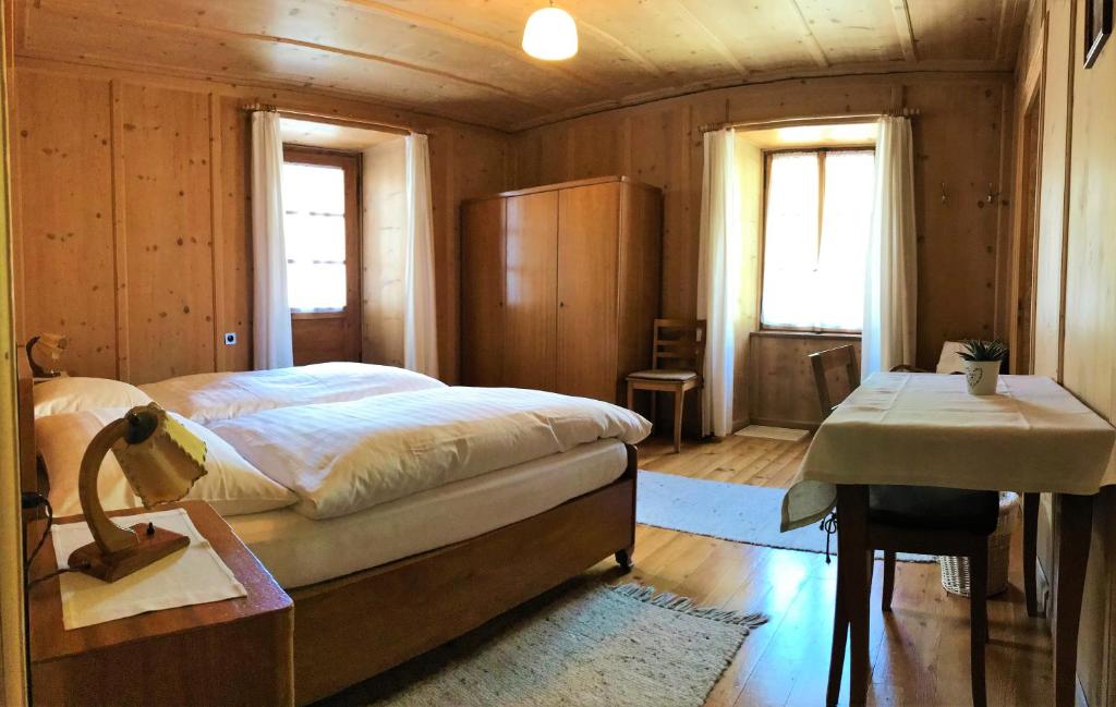 een slaapkamer met een bed, een bureau en 2 ramen bij Pensione Capelli in Prada