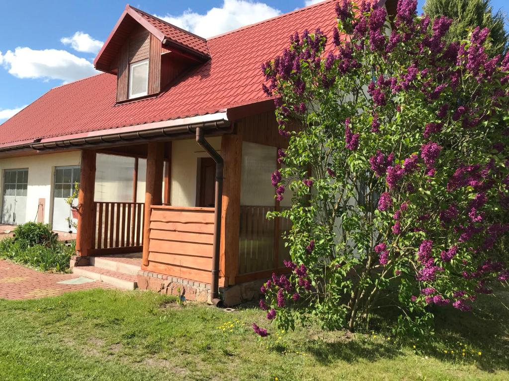 una casa con techo rojo y un arbusto con flores púrpuras en Miodunka en Dubicze Osoczne