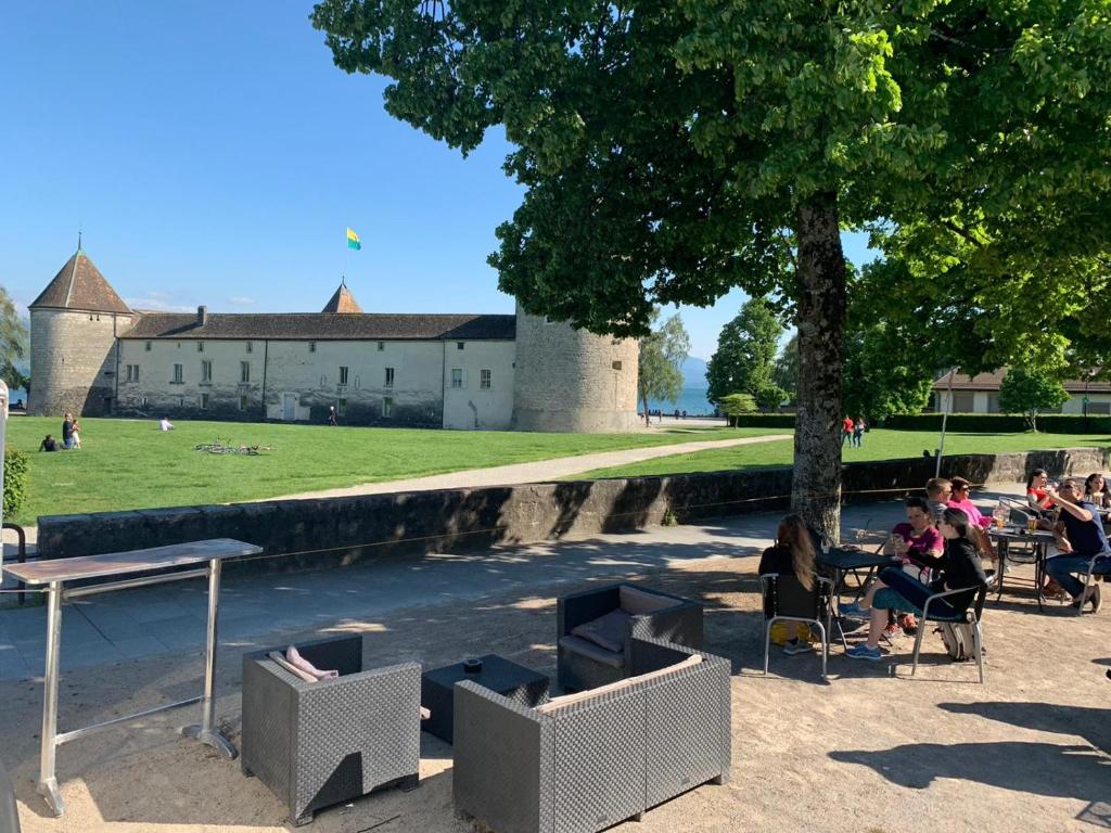 un groupe de personnes assises dans des chaises sous un arbre dans l'établissement L'Hôtel by Hostellerie du Château, à Rolle