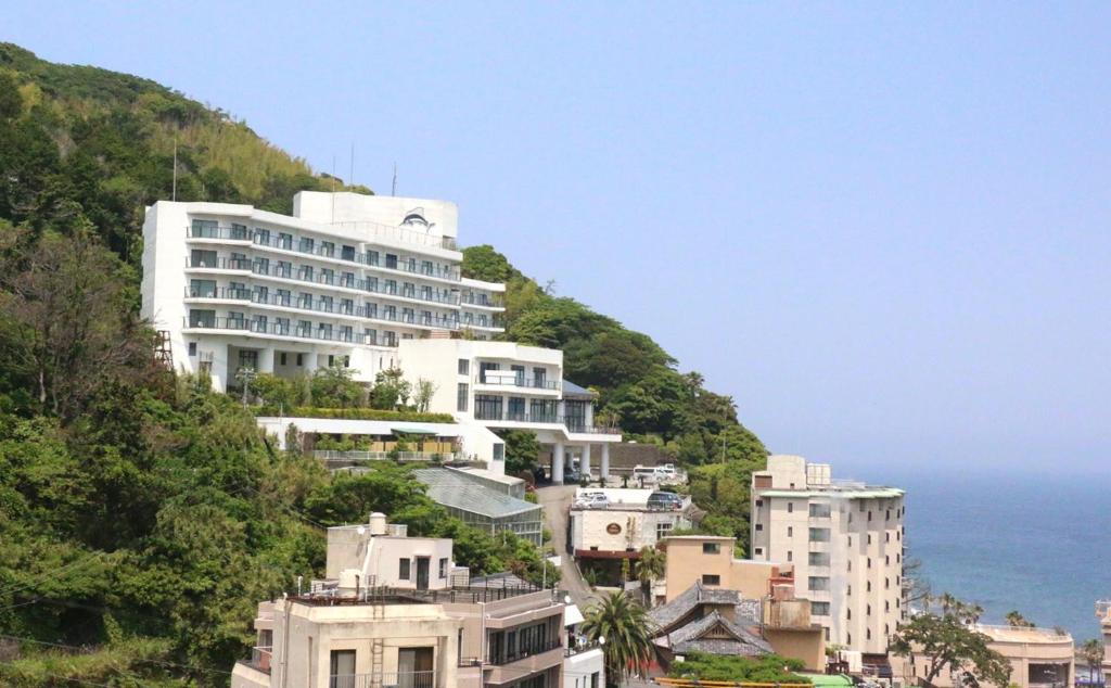 un grand bâtiment blanc sur une colline à côté de l'océan dans l'établissement Hotel Katara Resort & Spa, à Higashiizu