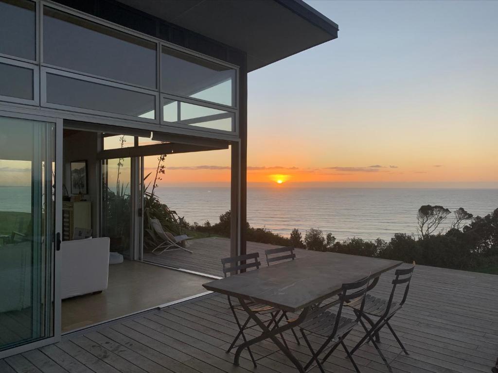 180° seaviews, superior coastal cottage في Waitoitoi: منزل به طاولة وكراسي على سطح مع غروب الشمس