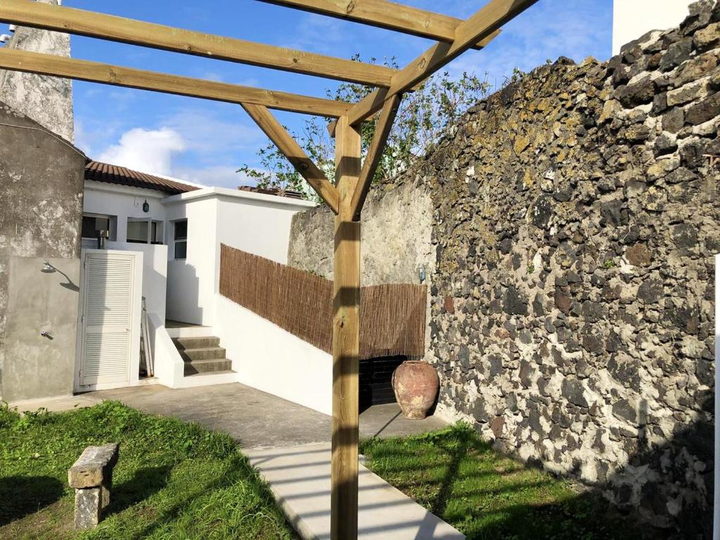 a building with a stone wall and a wooden pergola at 2 bedrooms house with city view enclosed garden and wifi at Ribeira Grande 1 km away from the beach in Ribeira Grande