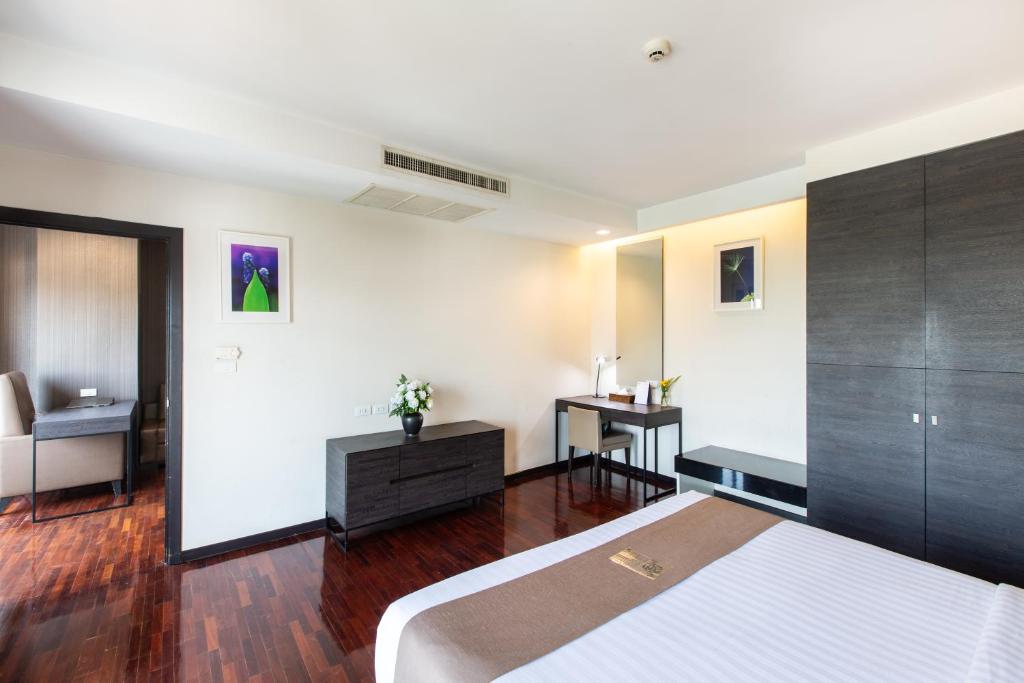 A bright bedroom with a partially visible bed, writing desk, wardrobe and separate sitting area.