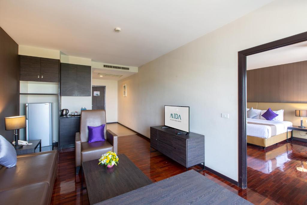 A suite living room with sofa, armchair, kitchenette and a view through to the separate bedroom.