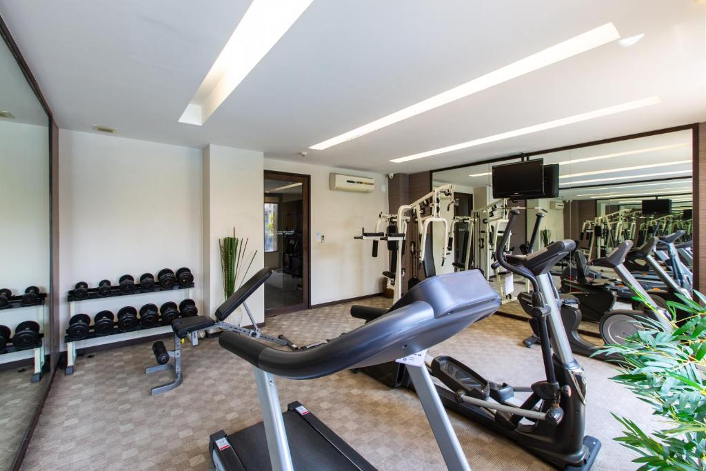 A compact mirrored gym with treadmills, bikes, a weight bench, dumbbells and a cable machine.