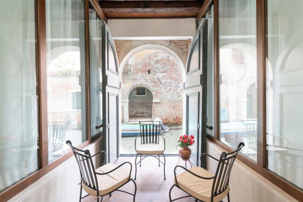 a porch with three chairs and a table with flowers at Riva Palace Apartments by Wonderful Italy in Venice