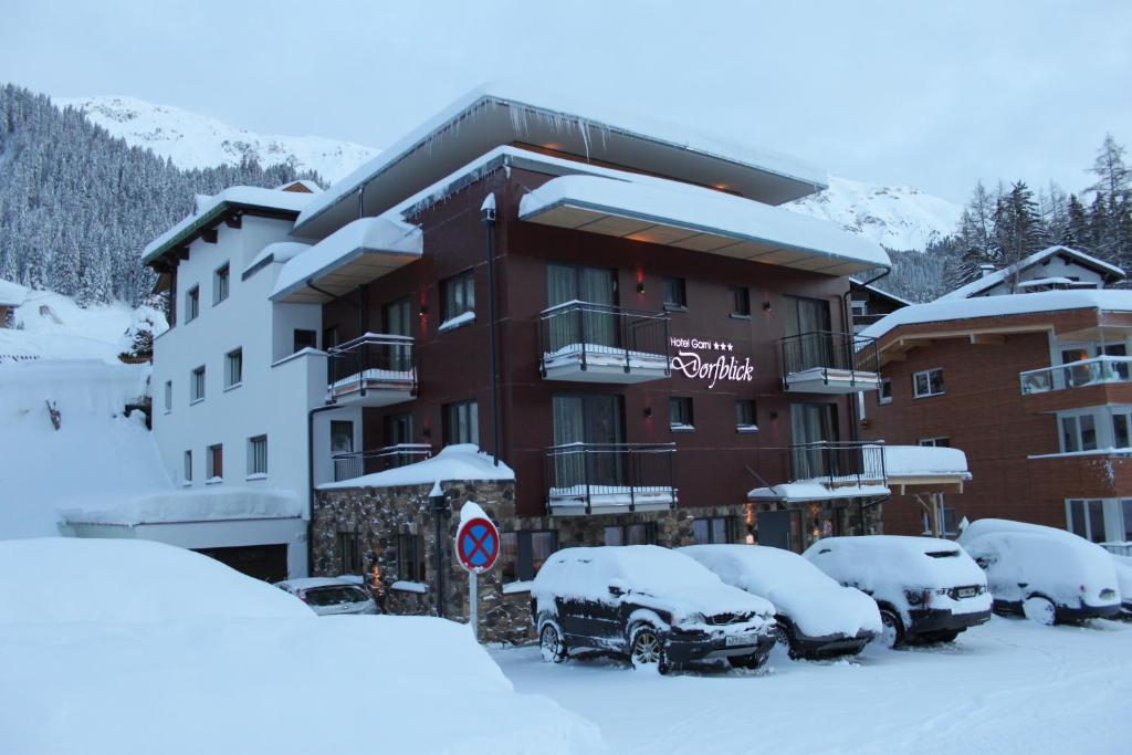 un bâtiment avec des voitures enneigées garées dans un parking dans l'établissement Hotel Garni Dorfblick, à Sankt Anton am Arlberg