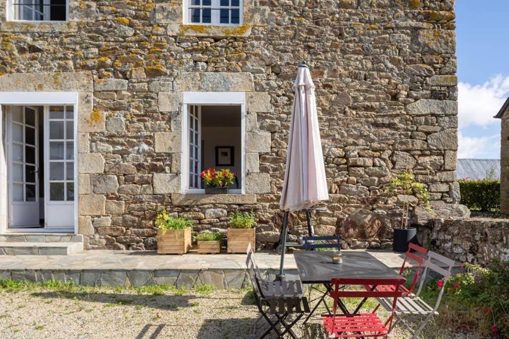 a table with an umbrella in front of a stone building at Maison de vacances en pierre entre terre et mer in Pluduno