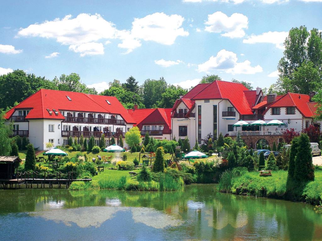 a building with red roofs next to a river at Bartlowizna Serce Biebrzy noclegi in Goniadz