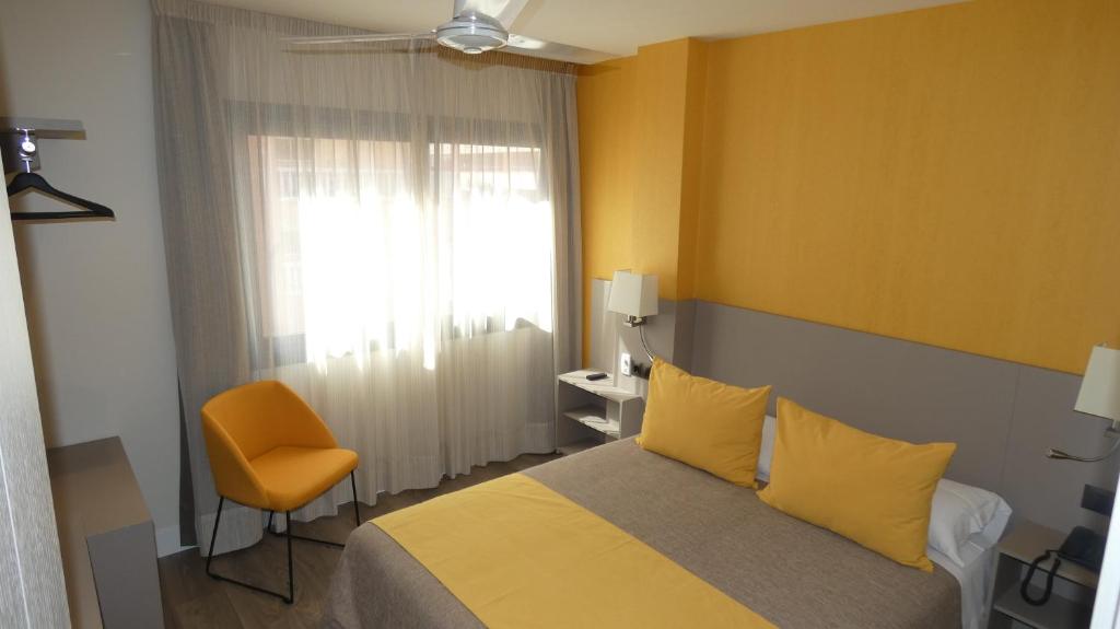 a bedroom with a bed and a chair and a window at Hotel Zeus in Málaga