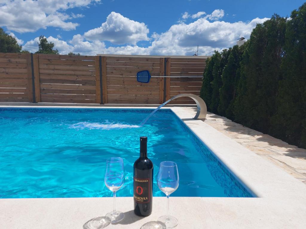 a bottle of wine and two wine glasses next to a swimming pool at Villa Belitzein with swimming pool in Šibenik