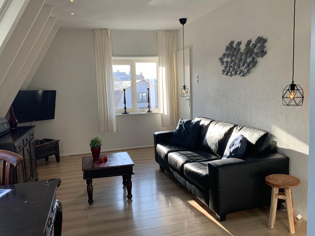 een woonkamer met een zwarte leren bank en een tafel bij Appartement Brouwer in Egmond aan Zee