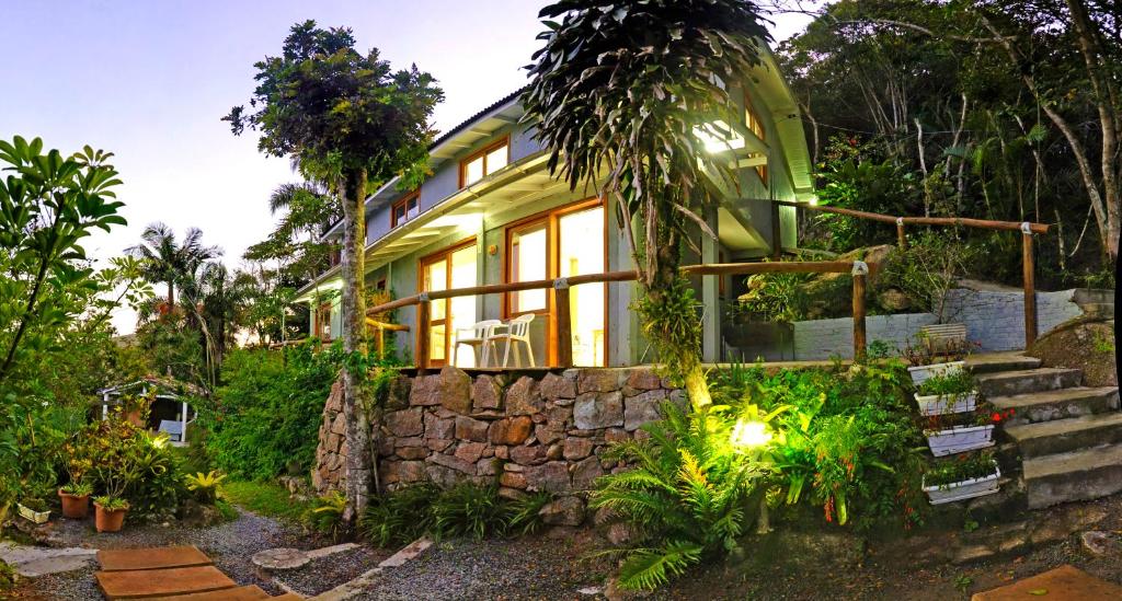 a green house with a stone wall and trees at Condomínio Aldeia dos Anjosdo Rosa in Praia do Rosa