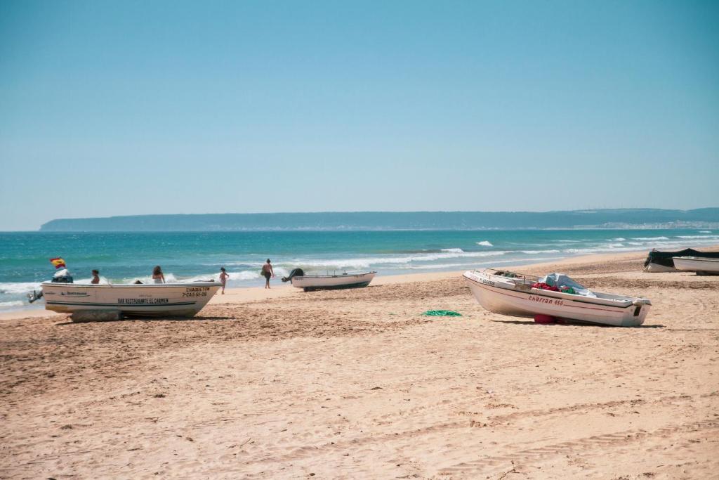 three boats on a beach with people in the water at Hotel Avenida Playa in Zahara de los Atunes
