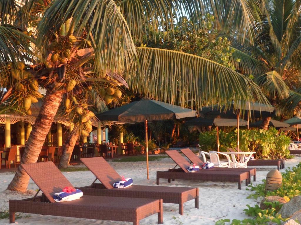 een rij ligstoelen en parasols op een strand bij Palm Beach Hotel in Grand'Anse Praslin