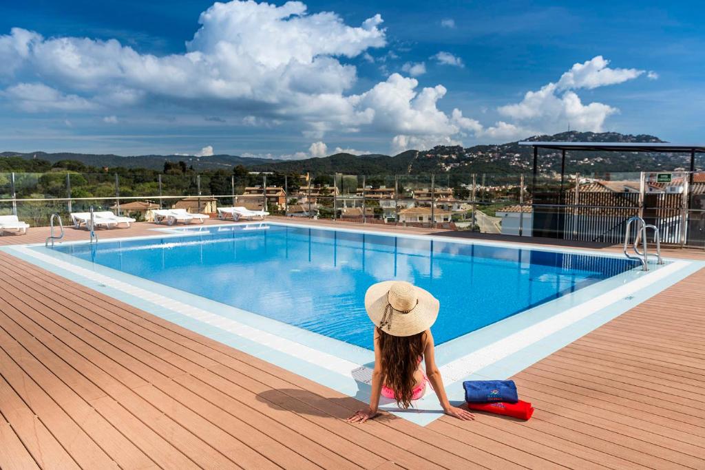 a girl in a hat sitting next to a swimming pool at Apartaments Condado in Lloret de Mar