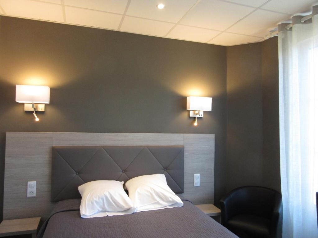 a bedroom with a bed with two pillows and two lights at Hotel de la Londaine in Champagnole